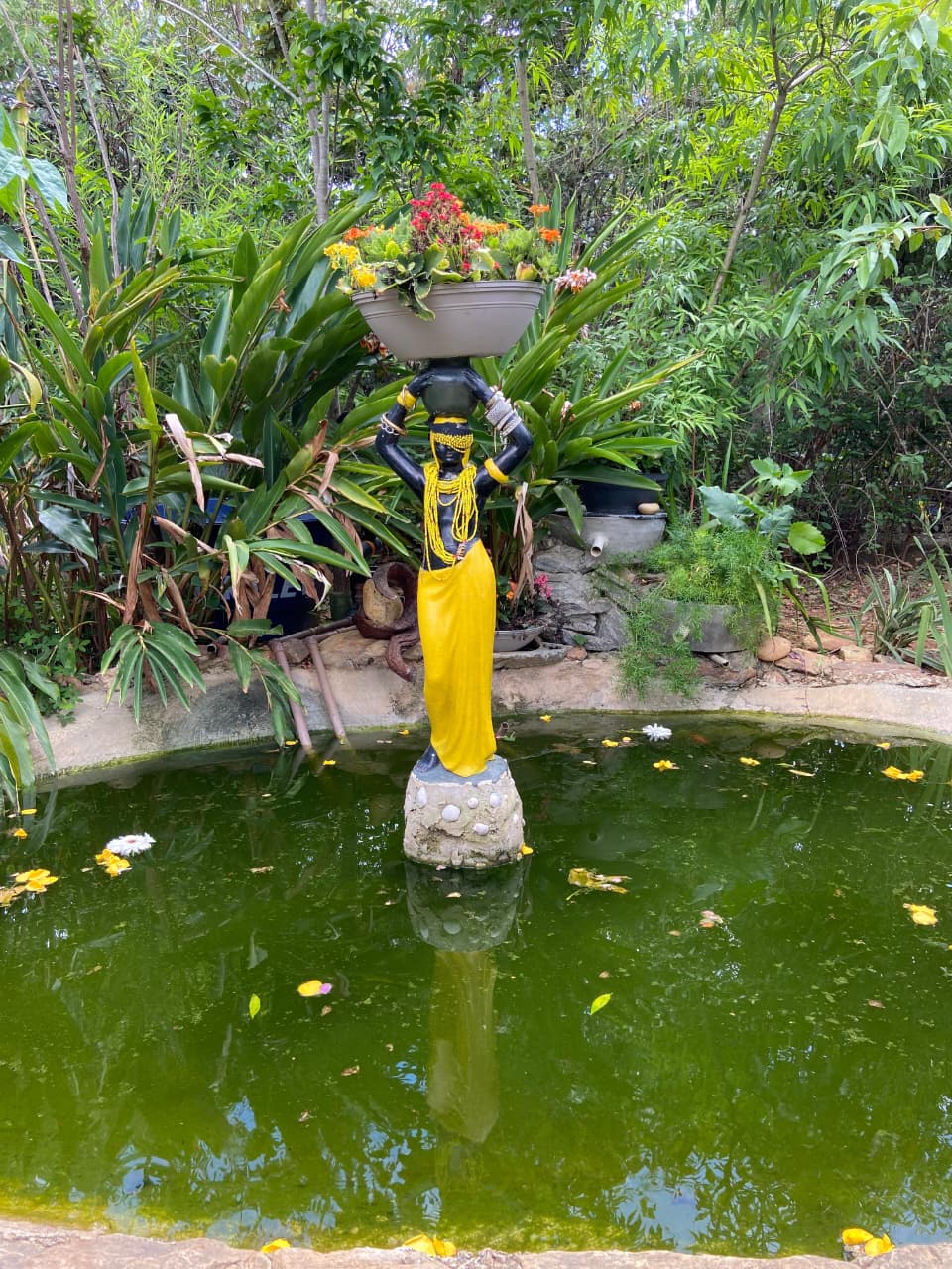 Escultura com flores no jardim da Roça Santo Antônio, diante do lago e cercada por folhagens